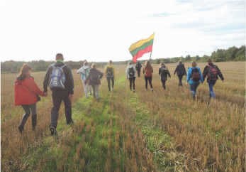 A group of students marching through the fields and carrying the Lithuanian flag.