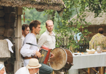 Men playing at an ancient house, one with an accordion and the other beating a drum.