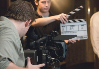 A student filming and other student holding a clap of film.