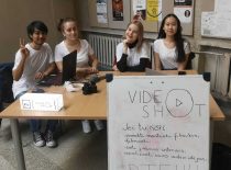 Trys merginos ir vienas vaikinas sėdi prie stalo su plakatu kviečiančiu stydentus prisijungti prie VideoShot organizacijos.