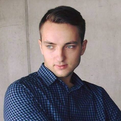 Trumpų, tamsių plaukų studentas, tamsiai mėlynos spalvos languotais marškiniai prie betoninės sienos.