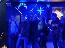 Mėlynai apšviestame kambaryje studentai žiūri ekspoziciją.