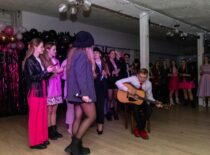 „Nemuno“ kolektyvo nariai mini Cementuko šventę, kurioje matomas vaikinas su gitara, mergina su mikrofonu ir būrys merginų už jų.
