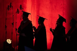 Mantijomis apsirengusių studentų šešėlis raudoname fone.