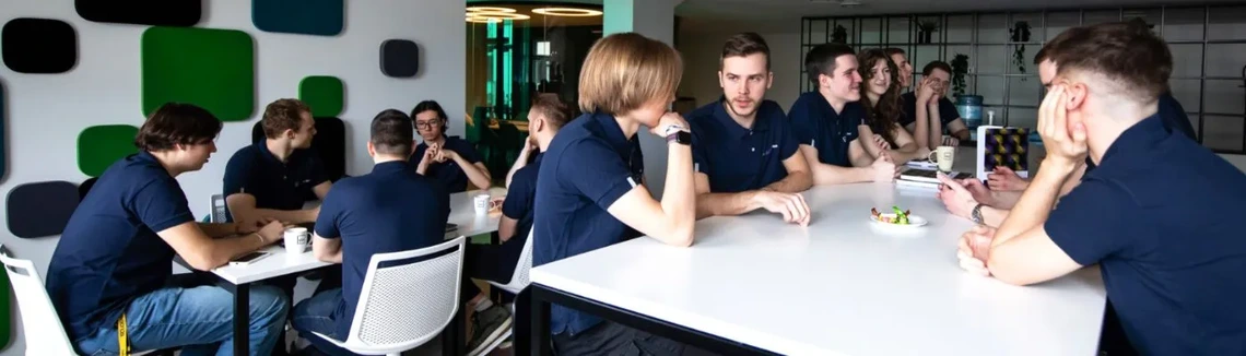 Daug studentų su SKILLed programos atributika sėdintys prie stalų, šnekasi