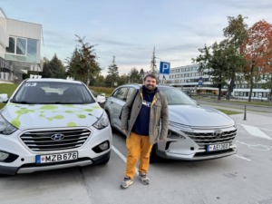 KTU mokslininkas B. G. Urbonavčius stovi tarp dviejų automobilių, &scaron;ypsosi