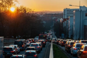 Didelė mašinų spūstis mieste, horizonte matosi saulė